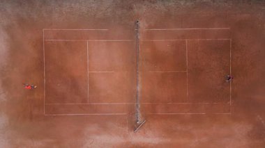 Çamur tenis kortunun havadan görünüşü, iki farklı tarafta iki oyuncu var. Simetrik bileşim beyaz sınır çizgileri, ağ ve desenli yüzey üzerindeki dağınık tenis toplarını vurgular.