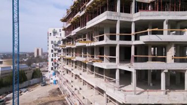 İnşaat halindeki vinçleri yüksek bir binanın havadan görüntüsü. Tamamlanmamış yapıda açık tuğlalar, beton sütunlar ve iskeleler var..