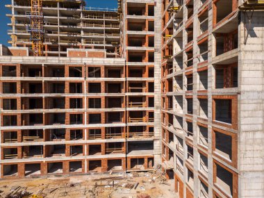 Güneşli bir günde yüksek katlı bir binanın inşaatı. Yapılar, beton iskelet, vinç ve iskelet parlak güneş ışığıyla yıkanarak kentsel gelişimi vurguluyor..