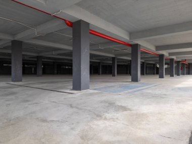 Beton sütunları ve açık kenarları olan boş bir yeraltı otoparkı. Endüstriyel alan doğal ışıkla aydınlanıyor, modern ama terk edilmiş bir atmosfer yaratıyor..
