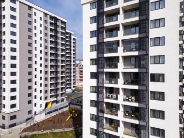 Şehir ortamında balkonları ve geniş pencereleri olan modern yüksek binalar. Avludaki renkli bir oyun parkı, aile dostu yaşam alanlarını vurguluyor..