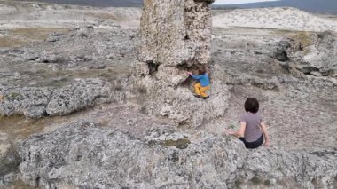 Bir anne engebeli bir arazide büyük bir kayaya tırmanırken çocuğunu destekler. Çocuk zorluğu keşfetmek için uzanır, anne ise rehberlik eder. Eşsiz bir kaya ile vahşi bir ortam.