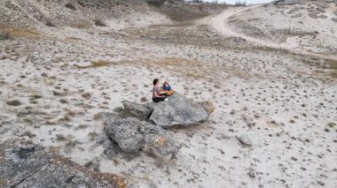 Bir anne ve çocuk kuru ve engebeli bir arazide bir kayanın üzerinde otururken meditasyon yapıyorlar. Rahatlamaya ve farkındalığa odaklanırlar, doğayla çevrili huzurlu bir anın tadını çıkarırlar..