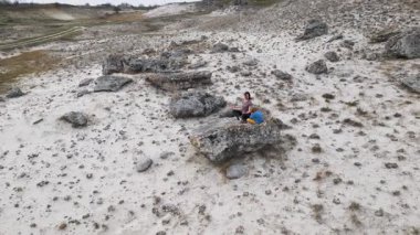 Bir anne ve çocuk kuru ve engebeli bir arazide bir kayanın üzerinde otururken meditasyon yapıyorlar. Rahatlamaya ve farkındalığa odaklanırlar, doğayla çevrili huzurlu bir anın tadını çıkarırlar..