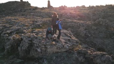 Bulutlu bir günde kayalık bir araziyi keşfeden kadın ve iki çocuk, kuru ve doğal bir ortamda yıpranmış taş oluşumlarının arasında yürüyorlar..