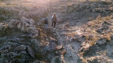 Bulutlu bir günde kayalık bir araziyi keşfeden kadın ve iki çocuk, kuru ve doğal bir ortamda yıpranmış taş oluşumlarının arasında yürüyorlar..