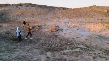 Kadın ve iki çocuk, altın saat boyunca kuru ve kayalık bir arazide planörlerle oynuyorlar. Açık havada eğleniyorlar ve ailecek vakit geçiriyorlar..