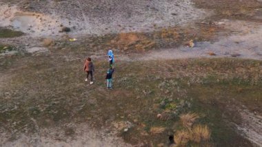 Kadın ve iki çocuk, altın saat boyunca kuru ve kayalık bir arazide planörlerle oynuyorlar. Açık havada eğleniyorlar ve ailecek vakit geçiriyorlar..