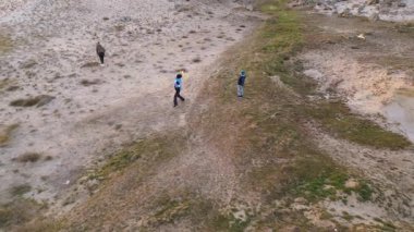 Kadın ve iki çocuk, altın saat boyunca kuru ve kayalık bir arazide planörlerle oynuyorlar. Açık havada eğleniyorlar ve ailecek vakit geçiriyorlar..