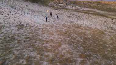 Kadın ve iki çocuk, altın saat boyunca kuru ve kayalık bir arazide planörlerle oynuyorlar. Açık havada eğleniyorlar ve ailecek vakit geçiriyorlar..