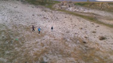 Kadın ve iki çocuk, altın saat boyunca kuru ve kayalık bir arazide planörlerle oynuyorlar. Açık havada eğleniyorlar ve ailecek vakit geçiriyorlar..