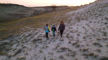 Kadın ve iki çocuk, altın saat boyunca kuru ve kayalık bir arazide planörlerle oynuyorlar. Açık havada eğleniyorlar ve ailecek vakit geçiriyorlar..