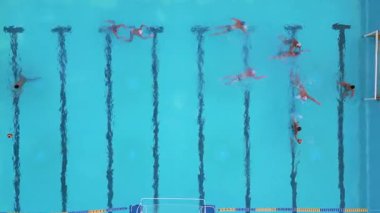 Bir su topu maçının hava görüntüsü devam ediyor, oyuncular açık mavi bir havuzda yüzüyor ve yarışıyorlar, her iki uçta da görünür hedefler var.