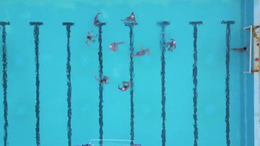 Bir su topu maçının hava görüntüsü devam ediyor, oyuncular açık mavi bir havuzda yüzüyor ve yarışıyorlar, her iki uçta da görünür hedefler var.