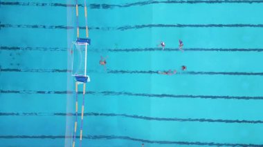 Yüzme havuzunda sutopu antrenmanının en üst görüntüsü. Oyuncular kalenin yanında top ve şerit işaretleriyle antrenman yapıyor..