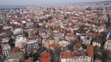 Bulgaristan 'ın Varna kentinin havadan görünüşü, açık bir gökyüzü altında kırmızı kiremitli çatıları, konut binaları ve kıyı arkaplanı olan yoğun bir şehir manzarasını gözler önüne seriyor..