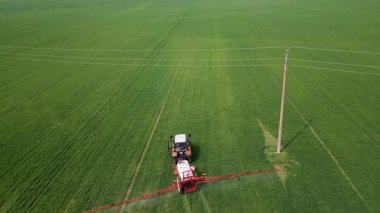 İlkbaharda geniş yeşil bir alana gübre ya da böcek ilacı püskürten traktör modern tarım teknolojisi ve mahsul bakımını gösteriyor..