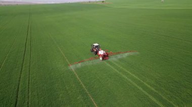 İlkbaharda geniş yeşil bir alana gübre ya da böcek ilacı püskürten traktör modern tarım teknolojisi ve mahsul bakımını gösteriyor..