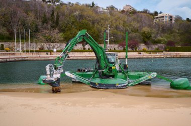 Deniz altı kazı ve onarım için kullanılan bir sahil ve su kanalının kenarında çalışan yeşil amfibik tarama makinesi marina veya kıyı bölgesi yakınında kullanılır..