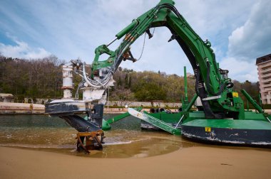 Deniz altı kazı ve onarım için kullanılan bir sahil ve su kanalının kenarında çalışan yeşil amfibik tarama makinesi marina veya kıyı bölgesi yakınında kullanılır..