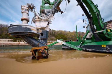 Deniz altı kazı ve onarım için kullanılan bir sahil ve su kanalının kenarında çalışan yeşil amfibik tarama makinesi marina veya kıyı bölgesi yakınında kullanılır..