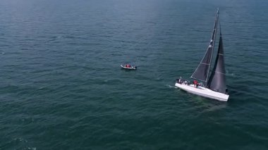 Kara yelkenli yelkenli bir yat bulutlu gökyüzünün altında uzak kıyı şeridinde, açık denizde seyrediyor..