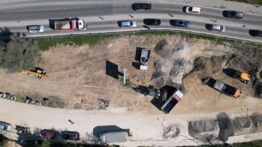 Kazı makineleri, kamyonlar, çakıl yığınları ve kavisli bir yoldaki trafiğin bulunduğu bir yol inşaatının havadan görüntüsü..