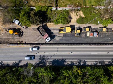 Ağır makineli yol şantiyesinin havadan görünüşü, güvenlik yelekli işçiler ve güneşli bir günde trafiği hareket ettirme.