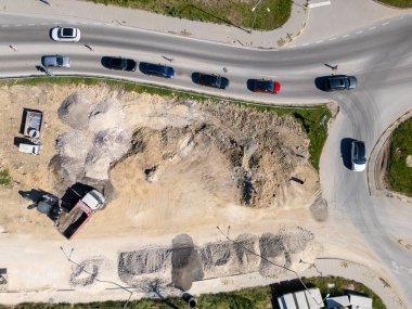 Ağır makineli yol şantiyesinin havadan görünüşü, güvenlik yelekli işçiler ve güneşli bir günde trafiği hareket ettirme.