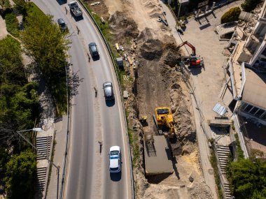 Ağır makineli yol şantiyesinin havadan görünüşü, güvenlik yelekli işçiler ve güneşli bir günde trafiği hareket ettirme.
