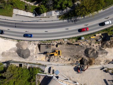 Ağır makineli yol şantiyesinin havadan görünüşü, güvenlik yelekli işçiler ve güneşli bir günde trafiği hareket ettirme.