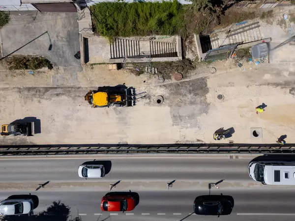 Ağır makineli yol şantiyesinin havadan görünüşü, güvenlik yelekli işçiler ve güneşli bir günde trafiği hareket ettirme.