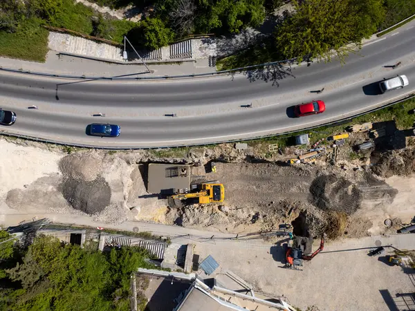 Ağır makineli yol şantiyesinin havadan görünüşü, güvenlik yelekli işçiler ve güneşli bir günde trafiği hareket ettirme.