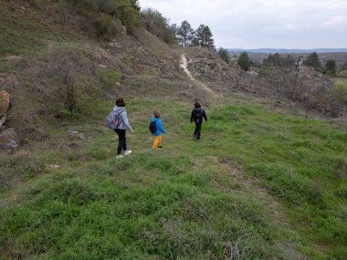 Anne ve iki çocuk bulutlu bir günde vahşi doğada yürüyüş yapıyorlar. Çalılarla ve kayalarla çevrili çimenli bir tepeye çıkıyorlar ve doğal bir çevrede birlikte vakit geçiriyorlar..