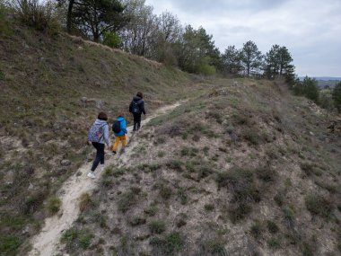 Anne ve iki çocuk bulutlu bir günde vahşi doğada yürüyüş yapıyorlar. Çalılarla ve kayalarla çevrili çimenli bir tepeye çıkıyorlar ve doğal bir çevrede birlikte vakit geçiriyorlar..