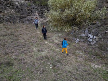 Anne ve iki çocuk bulutlu bir günde vahşi doğada yürüyüş yapıyorlar. Çalılarla ve kayalarla çevrili çimenli bir tepeye çıkıyorlar ve doğal bir çevrede birlikte vakit geçiriyorlar..