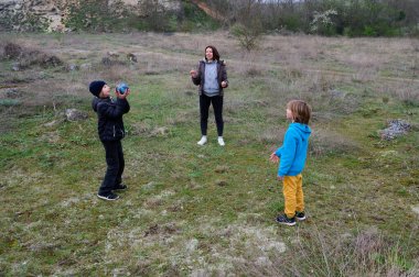 Anne ve iki çocuk çimenli bir arazide birlikte top oynuyorlar. Doğada aktif zaman geçirmeyi seviyorlar. Barışçıl ve doğal bir ortamda kaynaşıp eğleniyorlar..