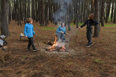 Anne ve iki çocuk ormanda bir kamp ateşinin yanında oturur, küçük bir masada yemek yer ve dinlenirler. Çam ağaçları ve doğa ile çevrili sıcak bir açık hava yemeğinden ve aile zamanından hoşlanırlar..