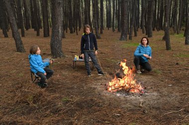 Anne ve iki çocuk ormanda bir kamp ateşinin yanında oturur, küçük bir masada yemek yer ve dinlenirler. Çam ağaçları ve doğa ile çevrili sıcak bir açık hava yemeğinden ve aile zamanından hoşlanırlar..