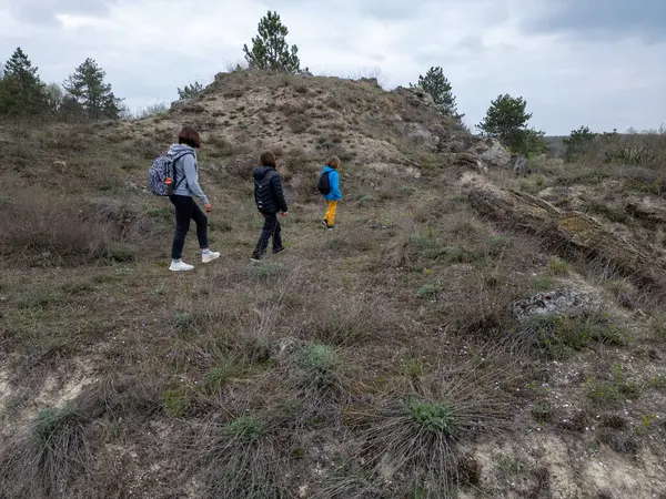 Anne ve iki çocuk bulutlu bir günde vahşi doğada yürüyüş yapıyorlar. Çalılarla ve kayalarla çevrili çimenli bir tepeye çıkıyorlar ve doğal bir çevrede birlikte vakit geçiriyorlar..