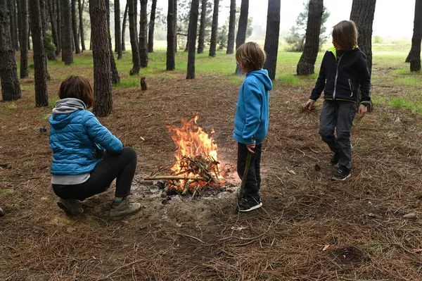 Anne ve iki çocuk ormanda bir kamp ateşinin yanında oturur, küçük bir masada yemek yer ve dinlenirler. Çam ağaçları ve doğa ile çevrili sıcak bir açık hava yemeğinden ve aile zamanından hoşlanırlar..