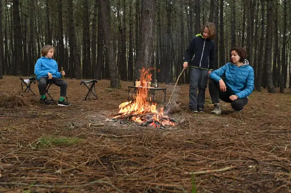Anne ve iki çocuk ormanda bir kamp ateşinin yanında oturur, küçük bir masada yemek yer ve dinlenirler. Çam ağaçları ve doğa ile çevrili sıcak bir açık hava yemeğinden ve aile zamanından hoşlanırlar..