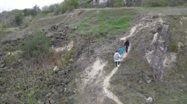 Anne ve iki çocuk bulutlu bir günde vahşi doğada yürüyüş yapıyorlar. Çalılarla ve kayalarla çevrili çimenli bir tepeye çıkıyorlar ve doğal bir çevrede birlikte vakit geçiriyorlar..