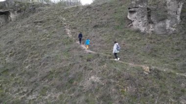 Anne ve iki çocuk bulutlu bir günde vahşi doğada yürüyüş yapıyorlar. Çalılarla ve kayalarla çevrili çimenli bir tepeye çıkıyorlar ve doğal bir çevrede birlikte vakit geçiriyorlar..