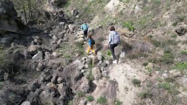 Anne ve iki çocuk, kayalar ve bahar bitkileriyle çevrili dar bir patika boyunca yokuş yukarı yürüyorlar. Güneşli bir günde, doğal bir ortamda huzurlu bir açık hava macerası..