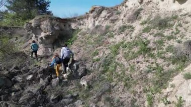 Anne ve iki çocuk, kayalar ve bahar bitkileriyle çevrili dar bir patika boyunca yokuş yukarı yürüyorlar. Güneşli bir günde, doğal bir ortamda huzurlu bir açık hava macerası..