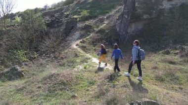 Anne ve iki çocuk, kayalar ve bahar bitkileriyle çevrili dar bir patika boyunca yokuş yukarı yürüyorlar. Güneşli bir günde, doğal bir ortamda huzurlu bir açık hava macerası..
