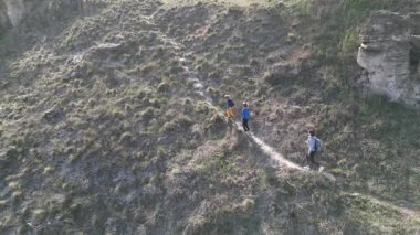 Anne ve iki çocuk, kayalar ve bahar bitkileriyle çevrili dar bir patika boyunca yokuş yukarı yürüyorlar. Güneşli bir günde, doğal bir ortamda huzurlu bir açık hava macerası..