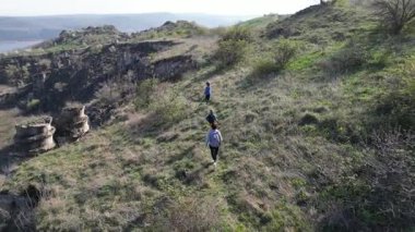 Güneşli bir günde bir anne ve iki çocuk manzaralı bir uçurumun kenarında yürüyüş yaparlar. Manzara engebeli ve vahşi, dramatik kaya oluşumları ve yeşil bahar bitkileriyle.