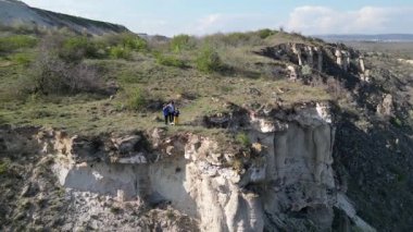 Güneşli bir günde bir anne ve iki çocuk manzaralı bir uçurumun kenarında yürüyüş yaparlar. Manzara engebeli ve vahşi, dramatik kaya oluşumları ve yeşil bahar bitkileriyle.